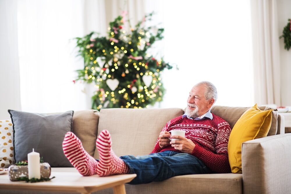 A senior man sitting on the couch with a Christmas sweater enjoying his cozy assisted living apartment