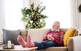 A senior man sitting on the couch with a Christmas sweater enjoying his cozy assisted living apartment